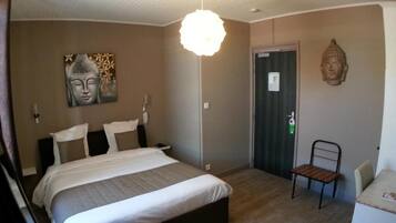 A bedroom with a bed, a chair, a Buddha statue, and a wall with a Buddha painting.