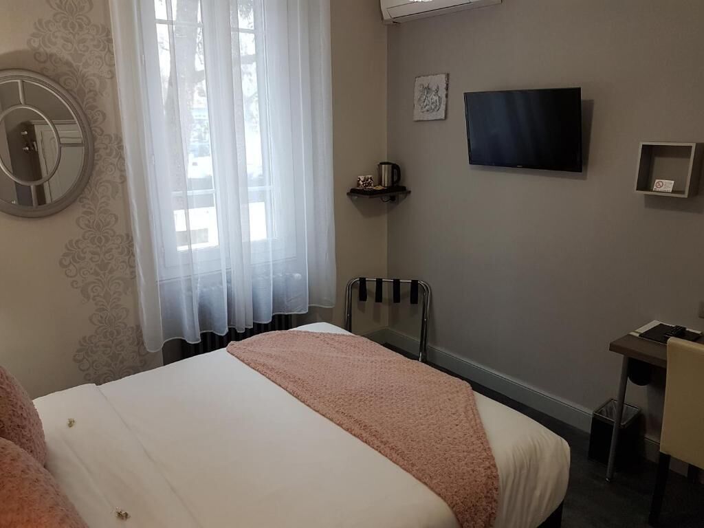 A hotel room with a bed, a chair, a desk, a TV, and a window with sheer curtains.