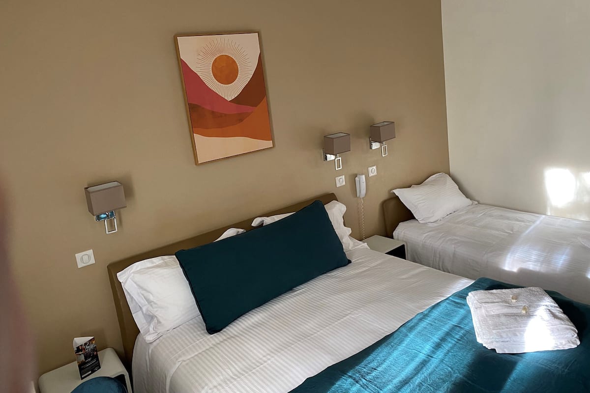A hotel room with two beds, a wall-mounted artwork, bedside lamps, a phone, and a small table with a magazine.