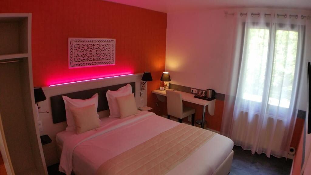 A hotel room with a bed, desk, and a window with curtains.