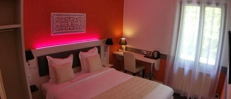 A hotel room with a bed, desk, and a window with curtains.