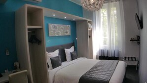 A bedroom with a bed, a wardrobe, a painting, a window with curtains, and a TV mounted on the wall. - Hôtel Beausoleil (Montélimar)