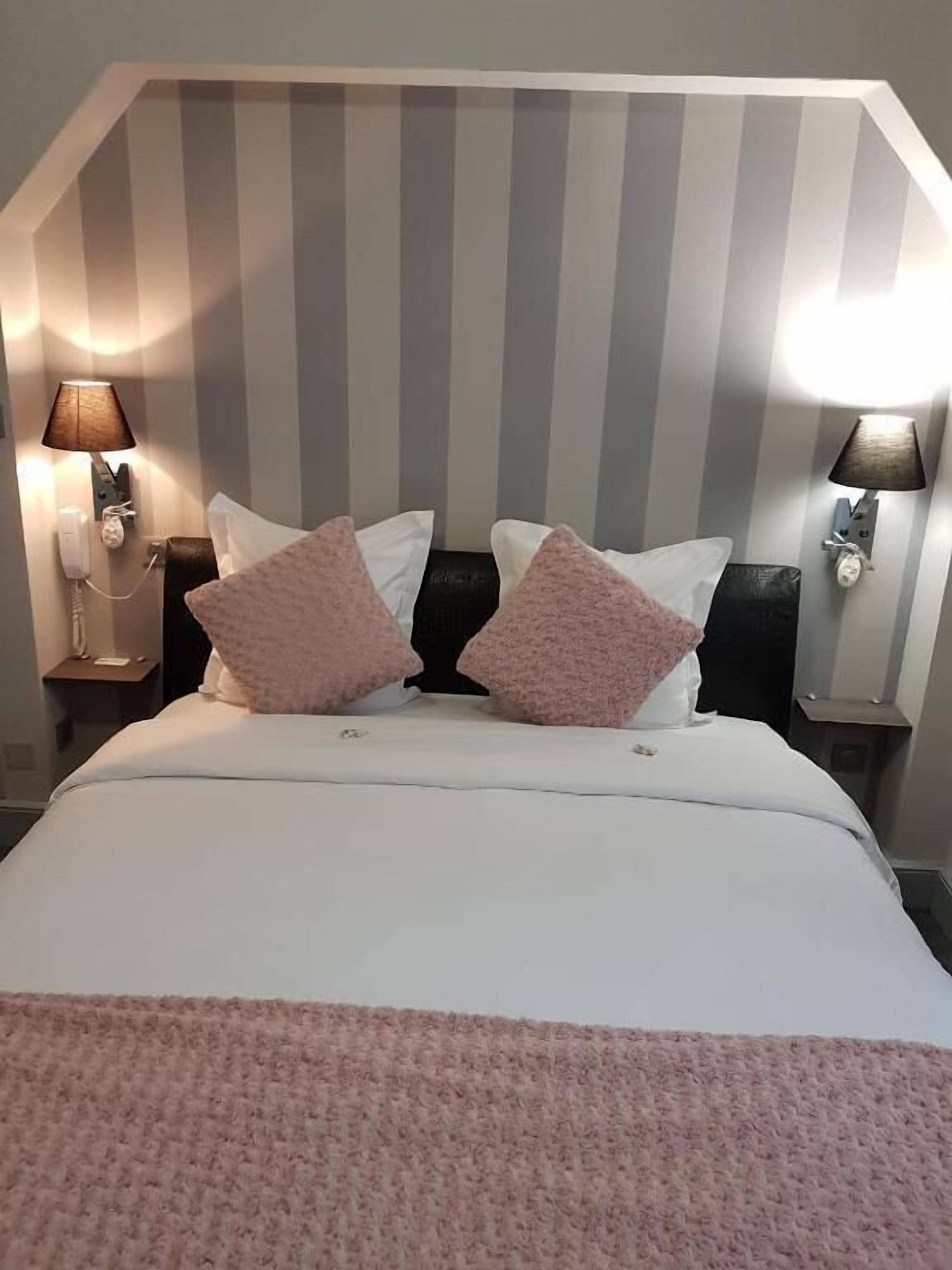 Une chambre d’hôtel avec un grand lit, deux lampes de chevet et un mur à rayures.