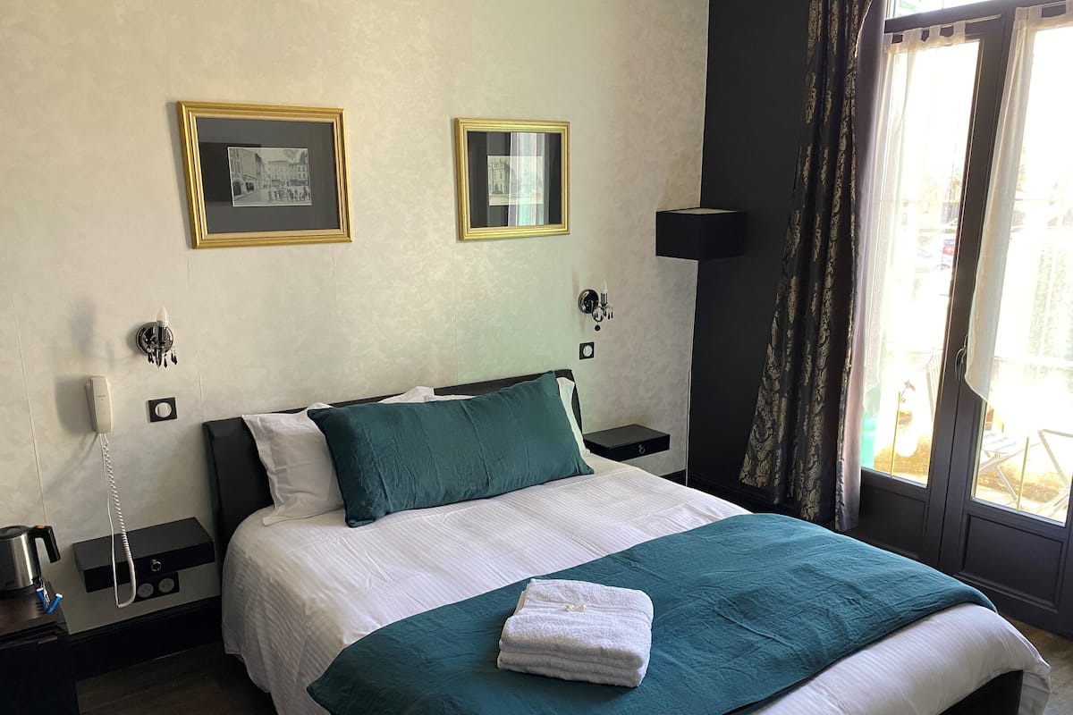 A hotel room with a bed, a bedside table with a lamp, a phone, and two framed pictures on the wall.