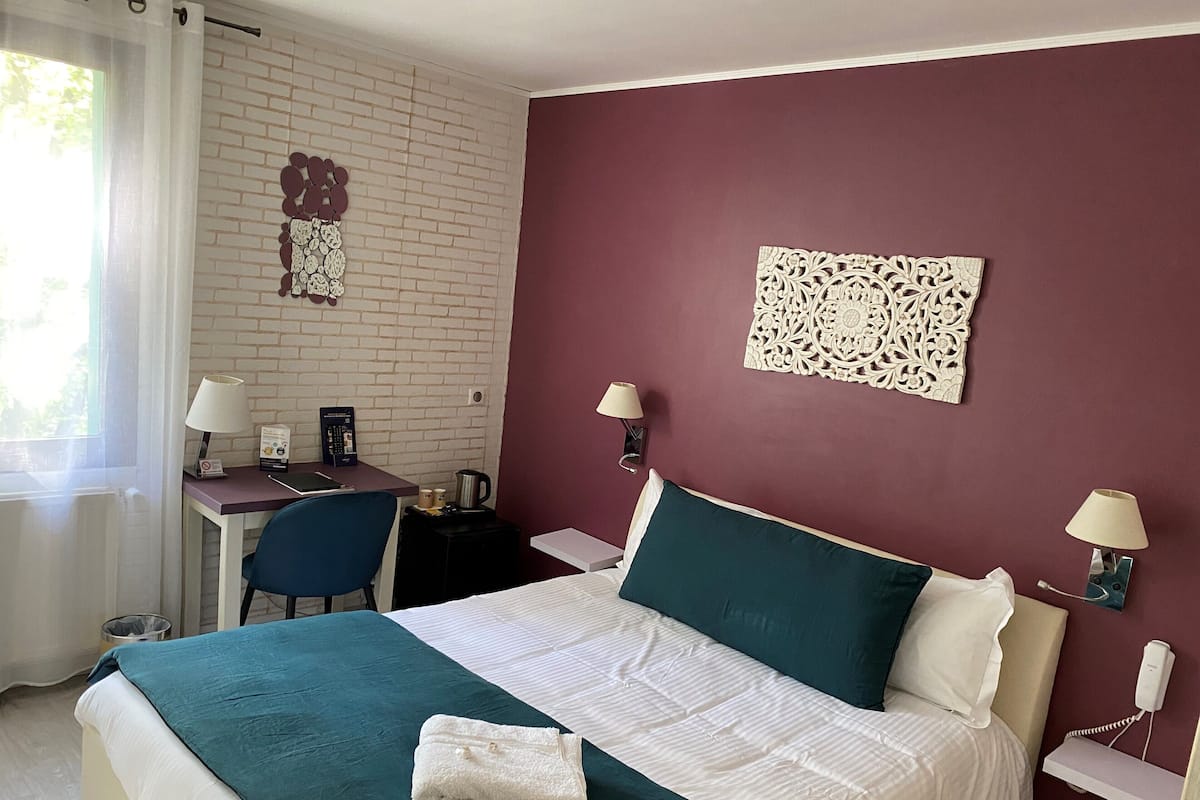 A hotel room with a bed, desk, chair, and two wall-mounted lamps.