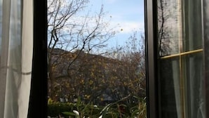 A view from a window with a table set with breakfast items, including oranges and a glass of orange juice, and a view of trees and a building in the background. - Hôtel Beausoleil (Montélimar)