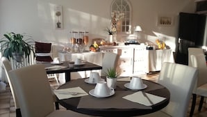 A dining area with a round table, white chairs, and a kitchen in the background. - Hôtel Beausoleil (Montélimar)
