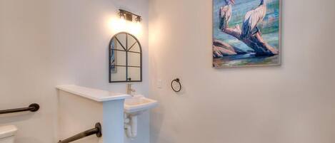 A bathroom with a white sink, a mirror with a black frame, a towel ring, and a painting of pelicans on the wall.