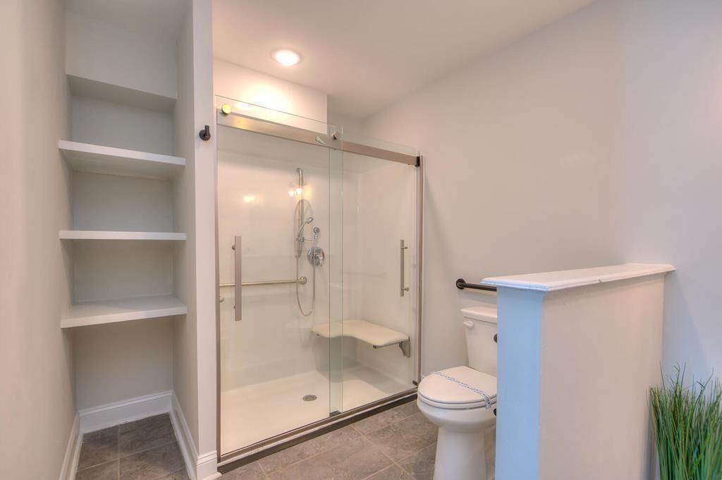 A modern bathroom with a glass-enclosed shower, a toilet, and built-in shelves.