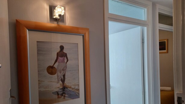 A framed photograph of a woman walking on a beach, a light fixture above it, and a partially open door leading to another room. - White Door Malt-Huku Kwetu (Dunstable) (Dunstable)