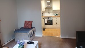 A compact living space with a kitchenette, a small seating area with a cushion, and a white table with a vase. - White Door Malt-Huku Kwetu (Dunstable) (Dunstable)