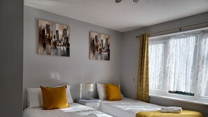 A hotel room with two single beds, a nightstand, a lamp, and two paintings on the wall. - White Door Malt-Huku Kwetu (Dunstable) (Dunstable)