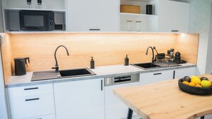 A modern kitchen with white cabinets, a wooden countertop, a built-in microwave, a sink with a faucet, and a small table with a fruit bowl.