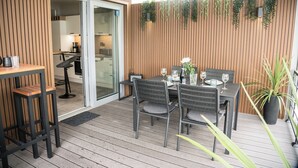 A wooden deck with a table set for dining, a bar area, and a sliding glass door leading to a kitchen.
