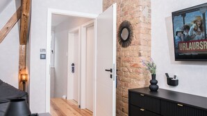 A modern interior with a wooden beam, a white door, a brick wall, and a black console with a mirror and a poster.
