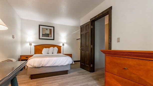 Une chambre à coucher avec un lit, des lampes de chevet, une commode en bois et une porte.