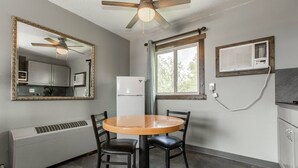 Une cuisine de taille réduite comprenant une table à manger, des chaises, un ventilateur de plafond, une fenêtre avec des rideaux et un climatiseur fixé au mur.