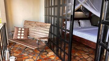 Una habitación con un banco de madera, una cama con mosquitero y suelo de piedra.