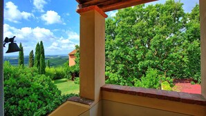 A balcony with a view of a lush garden, a bell, and a building with a red roof. - Villa Marliana - Luxury Villa with private pool (Cerreto Guidi)