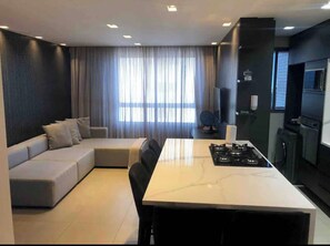 Uma sala de estar moderna com um sofá seccional, uma mesa de jantar e uma área de cozinha com fogão.