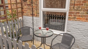 A patio with two wicker chairs, a small round table, and two glasses of red wine.