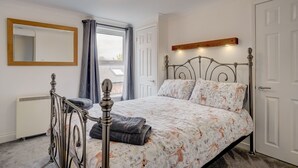 A bedroom with a metal bed frame, a large mirror, a radiator, and a window with curtains.