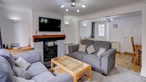 A living room with a fireplace, grey sofas, a coffee table, and a flat-screen TV mounted on the wall.