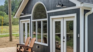 Un bâtiment à l’extérieur sombre, avec des éléments décoratifs blancs et de grandes fenêtres en arc de cercle. On peut voir deux chaises en bois sur une terrasse à l’avant.