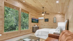 Une pièce de cabane en bois comprenant un lit, une table, un canapé et une grande fenêtre donnant sur la forêt.