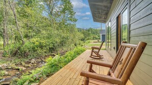 A wooden deck with rocking chairs overlooking a stream and forest.