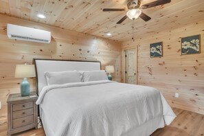Ein Schlafzimmer mit Holzvertäfelung, einem Bett, Nachttischen, Lampen und einem Deckenventilator.