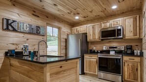 Une cuisine en bois dotée d’un îlot central, d’appareils électroménagers en acier inoxydable et offrant une vue sur l’extérieur.