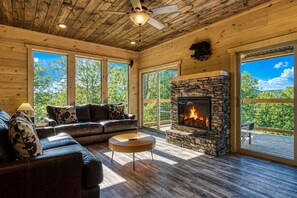 L’intérieur d’une cabane en rondins, avec une cheminée en pierre, un canapé en cuir et de grandes fenêtres.