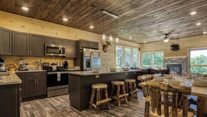 Une cuisine rustique avec un plancher en bois, un îlot central doté de tabourets et une cheminée en pierre.