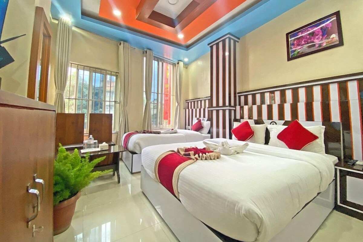 A hotel room with two beds, a desk, a TV, and a large window.