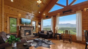 Ein Blockhaus-Interieur mit Kamin, Ledersofa und Blick auf die Berge.
