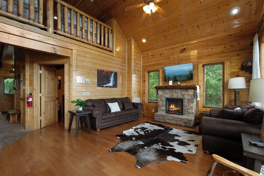 A wooden cabin interior with a fireplace, leather sofa, and a cowhide rug.