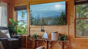 Ein Holzblockhaus-Innenraum mit großem Fenster, einer Couch, einem Tisch und Topfpflanzen.
