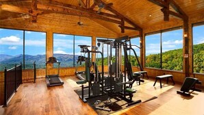 Ein Fitnessraum mit Trainingsgeräten und großen Fenstern mit Blick auf eine gebirgige Landschaft.