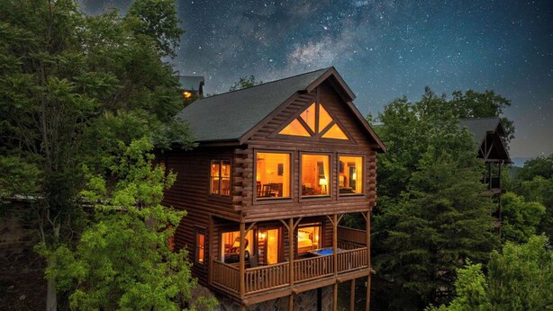 Eine Holzhütte mit Balkon, umgeben von Bäumen, unter einem sternenübersäten Nachthimmel.
