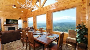 A wooden cabin interior with a dining table, chairs, a fireplace, and large windows offering a mountain view. - Starry Starry Night: Count Stars, Not Worries (Sevierville)