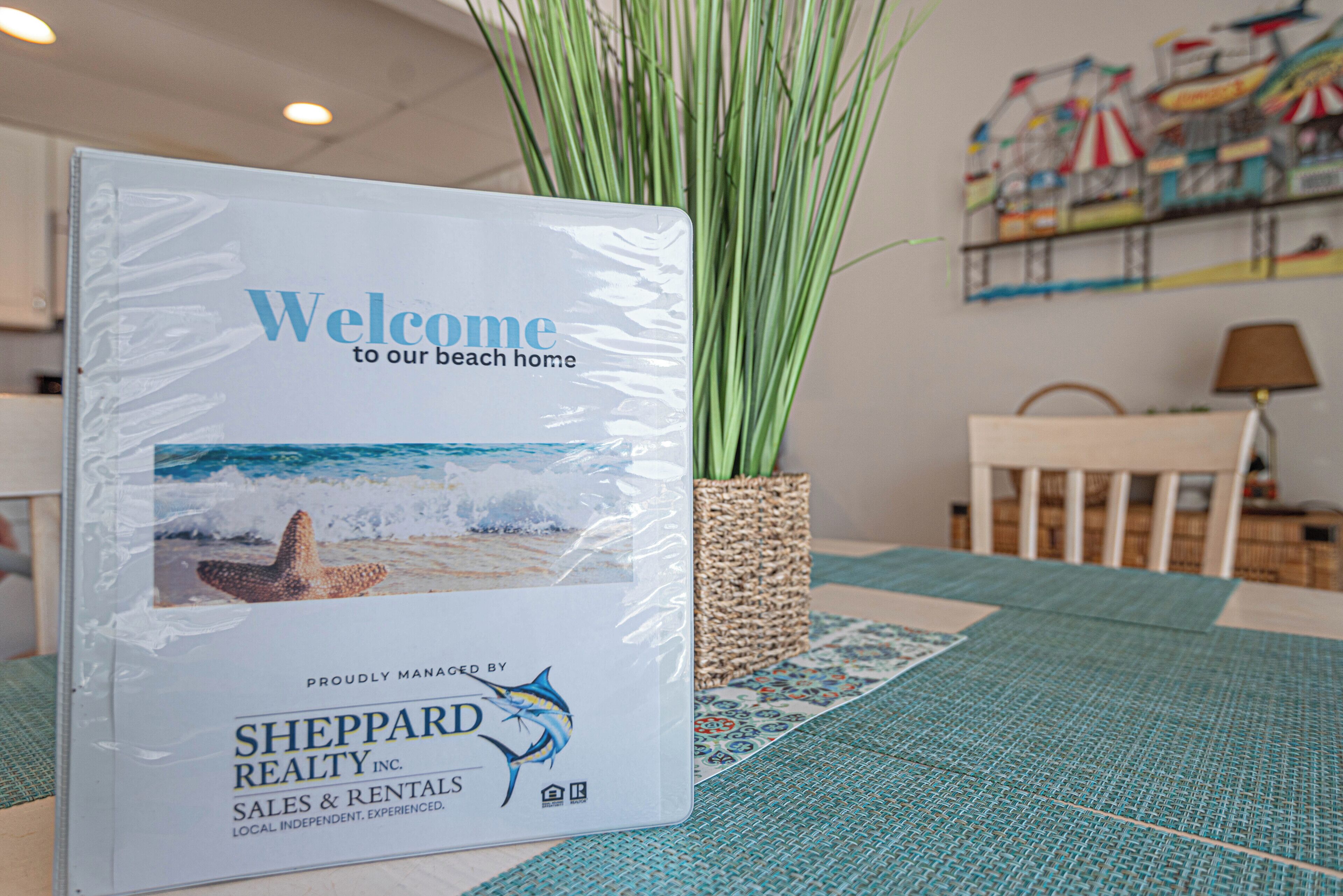 Un cartel de bienvenida para una casa de playa, una cesta tejida y una mesa con mantel tejido.