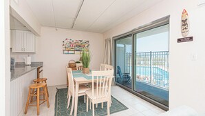 Een eetgedeelte met een tafel voor vier personen, een keuken met witte kasten en uitzicht op een zwembad door een glazen deur.