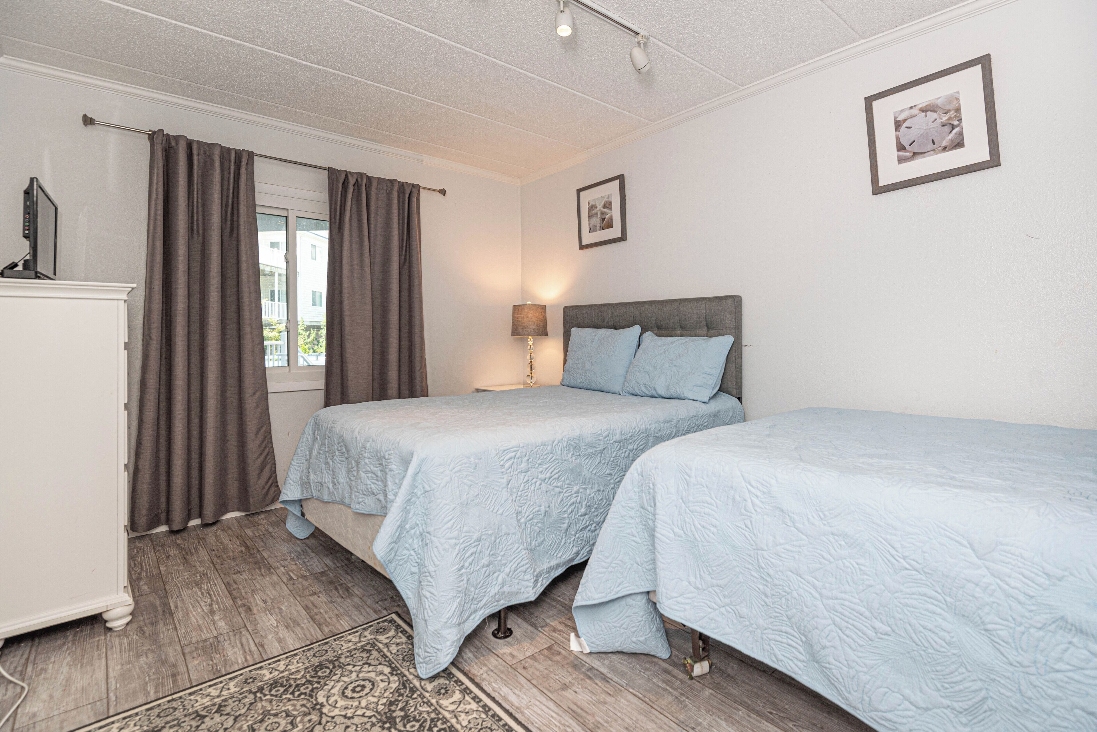 Een slaapkamer met twee bedden, een nachtkastje, een lamp en een raam met gordijnen.