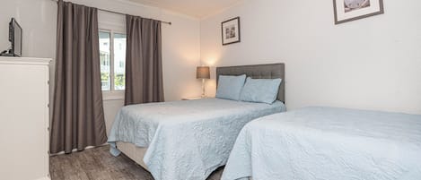 Een slaapkamer met twee bedden, een nachtkastje, een lamp en een raam met gordijnen.