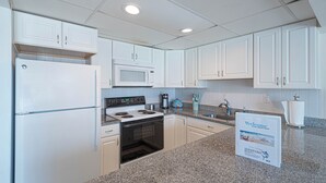 Een keuken met witte kastjes, een koelkast, een magnetron, een oven en een spoelbak. Op het aanrecht staat een welkomstbord.