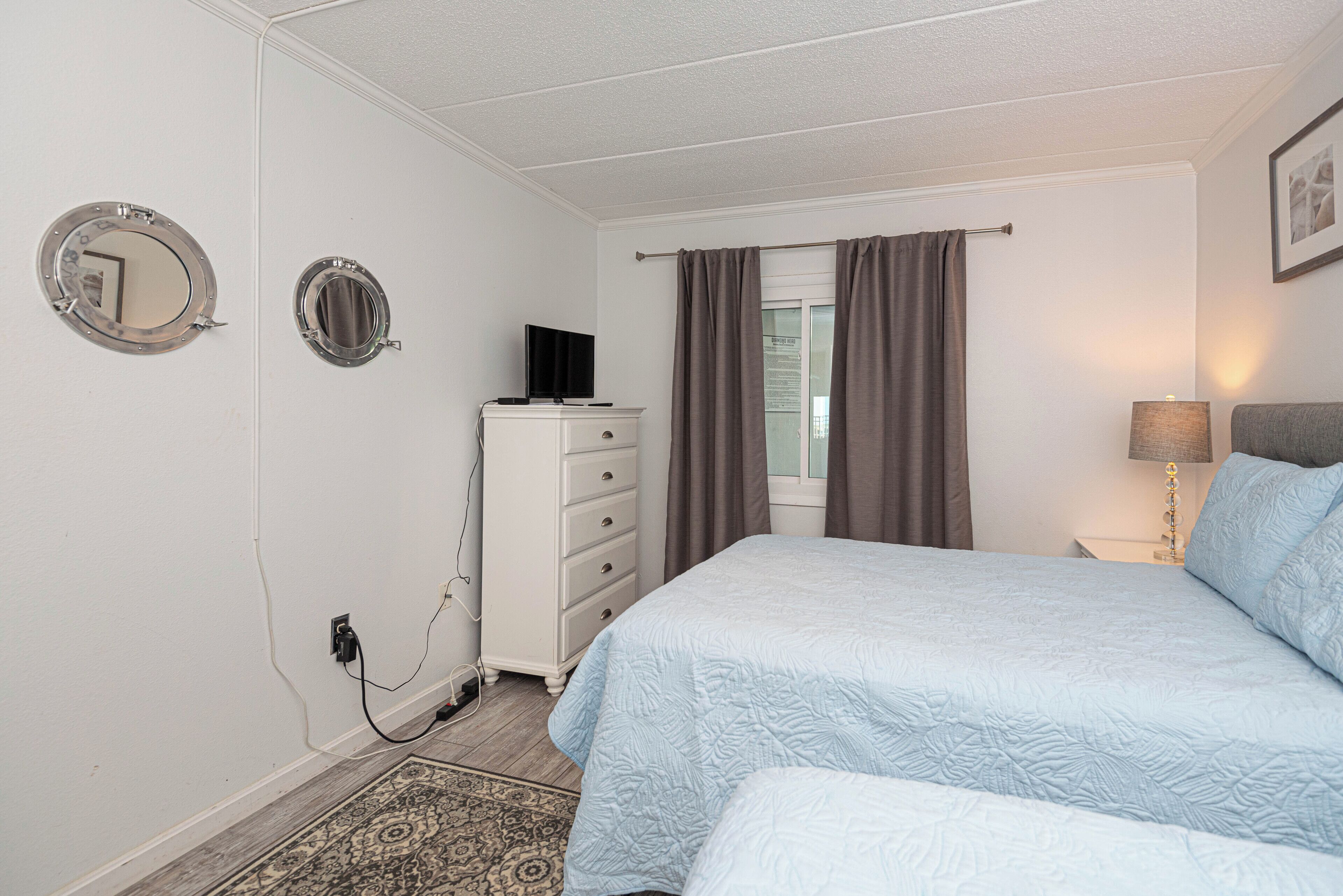 A bedroom with two beds, a dresser, a television on the dresser, and a window with curtains.