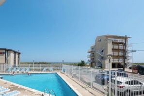 A swimming pool with lounge chairs and a fenced area, adjacent to a multi-story building with balconies. - Large Ocean Front 2bed/2bath with pool. A perfect fit for large family! Sleep 10 (Ocean City)