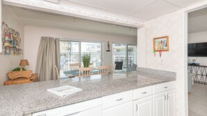 Een moderne keuken met witte kasten, een granieten aanrechtblad en een eethoek met een tafel en stoelen.