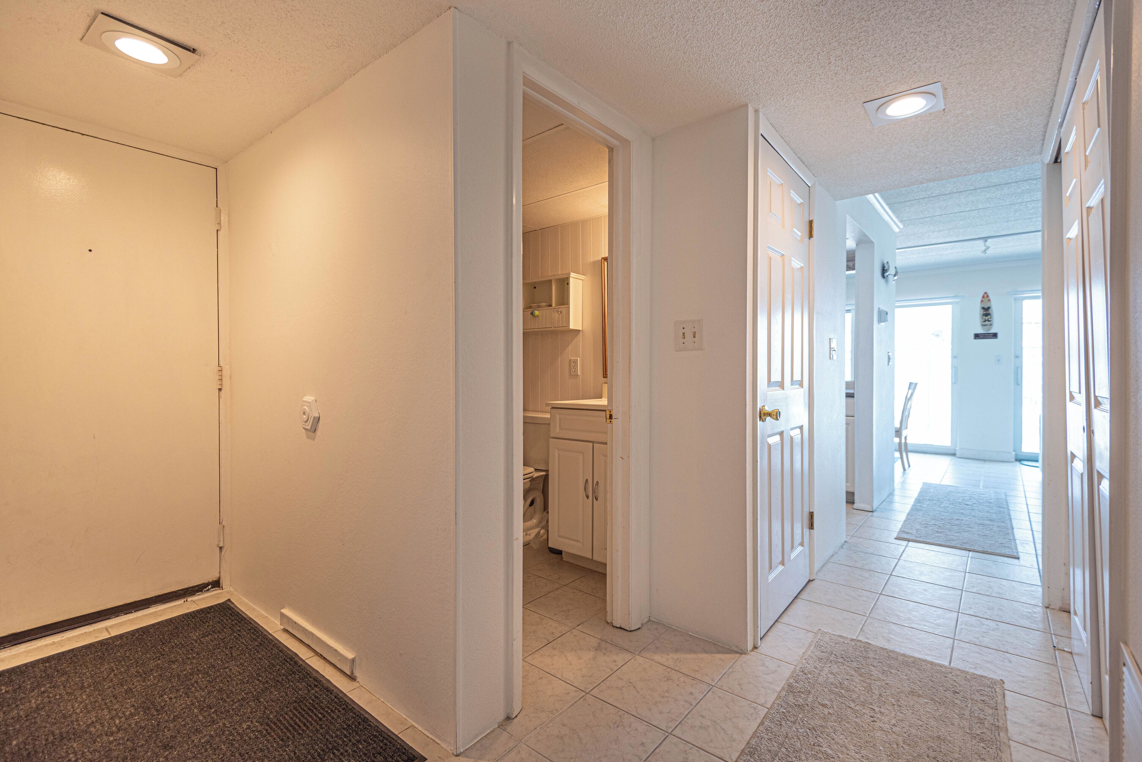 A hallway with a carpeted entrance, leading to a kitchen area with cabinets and a refrigerator.